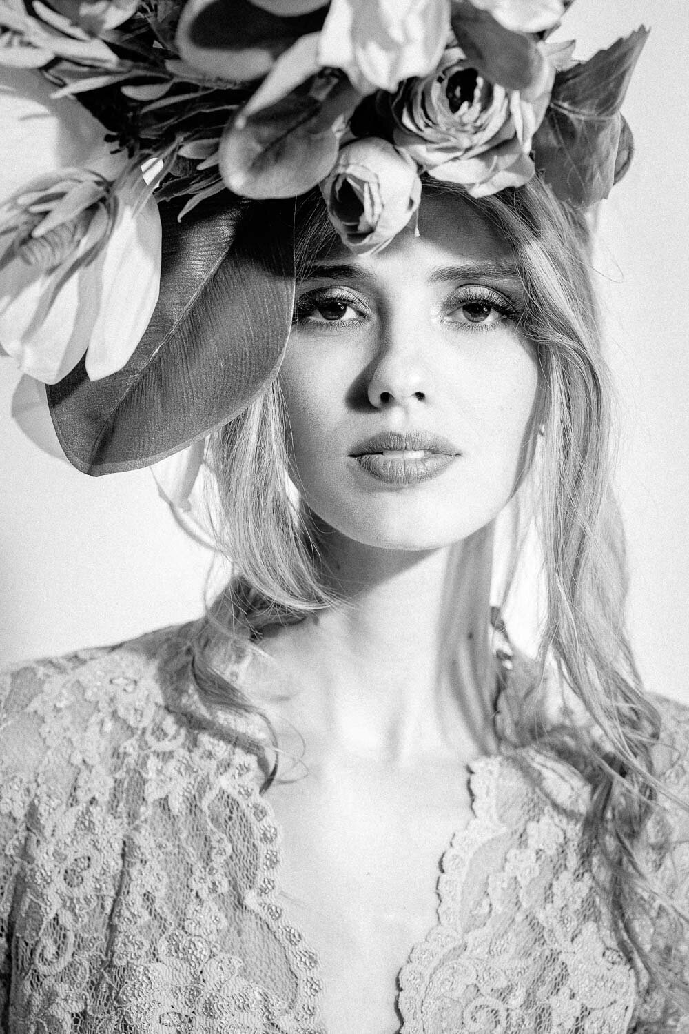 Black and white close-up beauty portrait of a woman wearing a floral crown and lace dress, captured on a clean white backdrop with subtle film grain in Austin, TX.