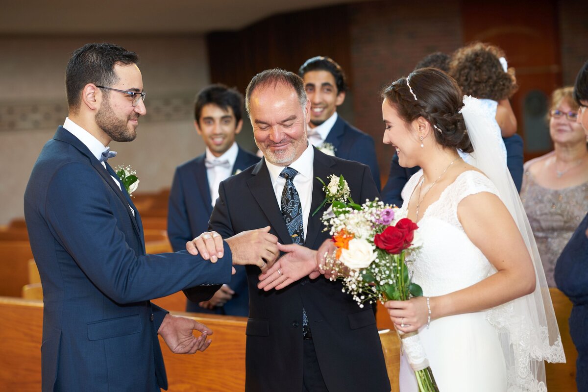 The father walks the bride down the aisle, handing her over to the groom in a touching moment of tradition and emotion. This image captures the poignant and heartfelt exchange, highlighting the significance of the father’s role and the couple’s commitment to each other during the wedding ceremony.