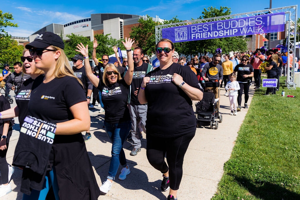 People walk on a path with a sign behind that says "Best Buddies Friendship Walk."