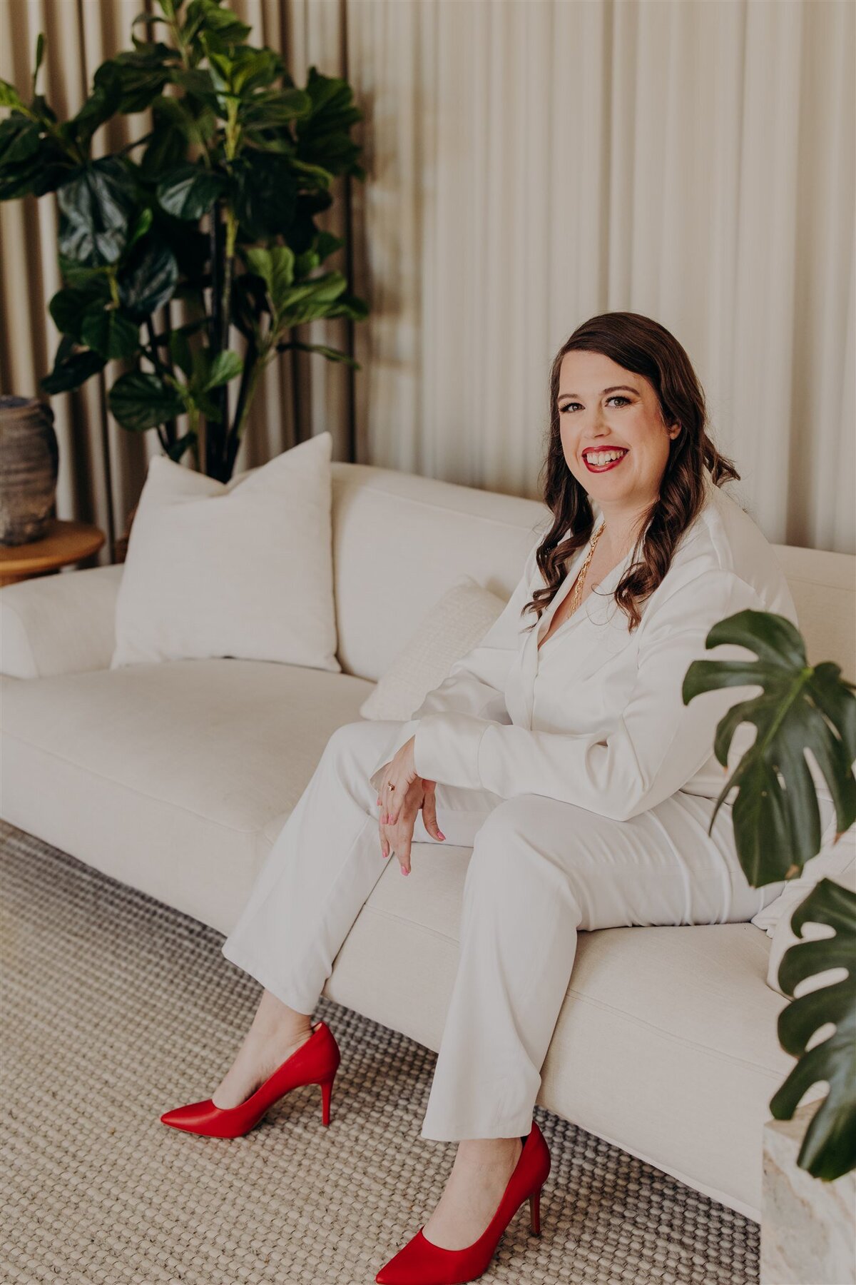 therapist in white suit sitting on couch with hands folded and smiling