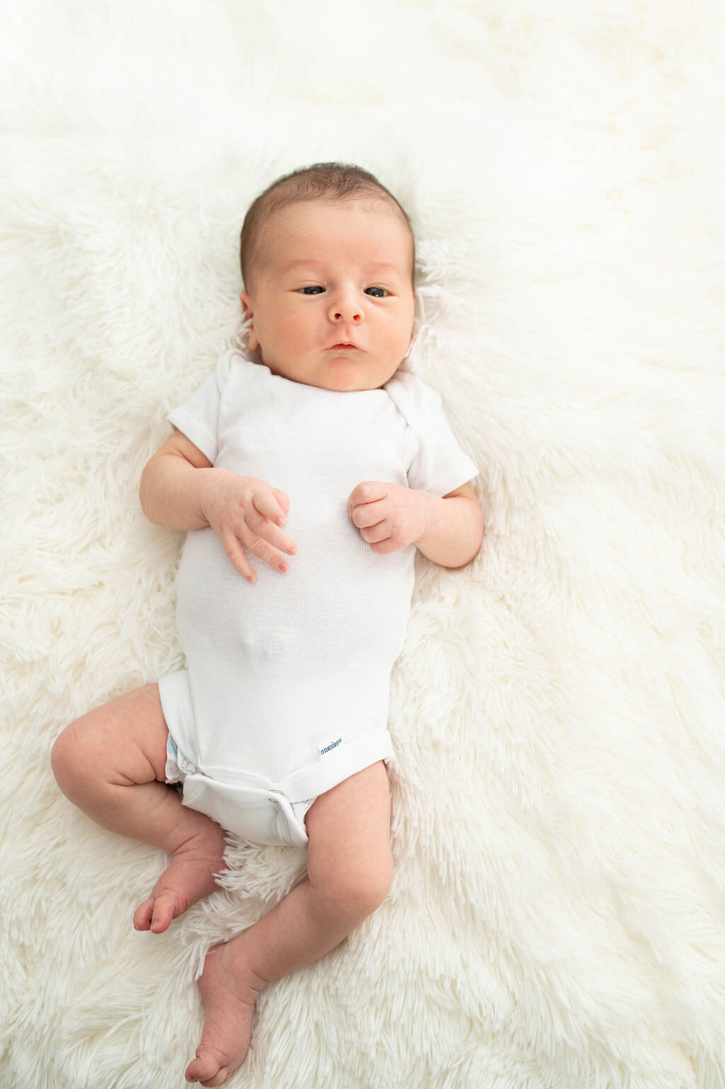 A newborn baby in a onesie laying on a blanket.