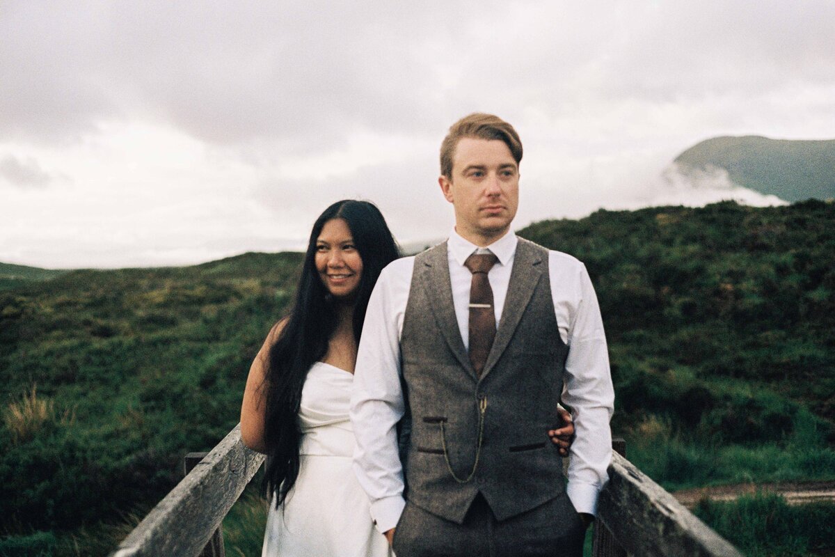 A bride and groom are photographed side by side on a bride. They look opposite directions and an open Aberdeenshire landscape is seen around them.