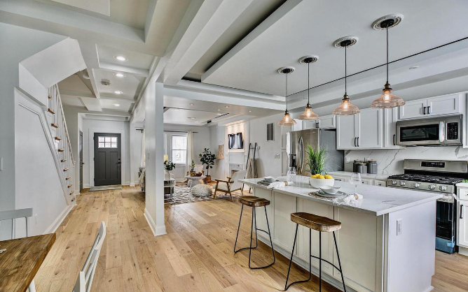 Spacious open-concept renovation featuring a quartz island with seating, custom cabinetry, pendant lighting, and wide-plank hardwood floors—seamlessly connecting the kitchen, dining, and living areas for modern living.