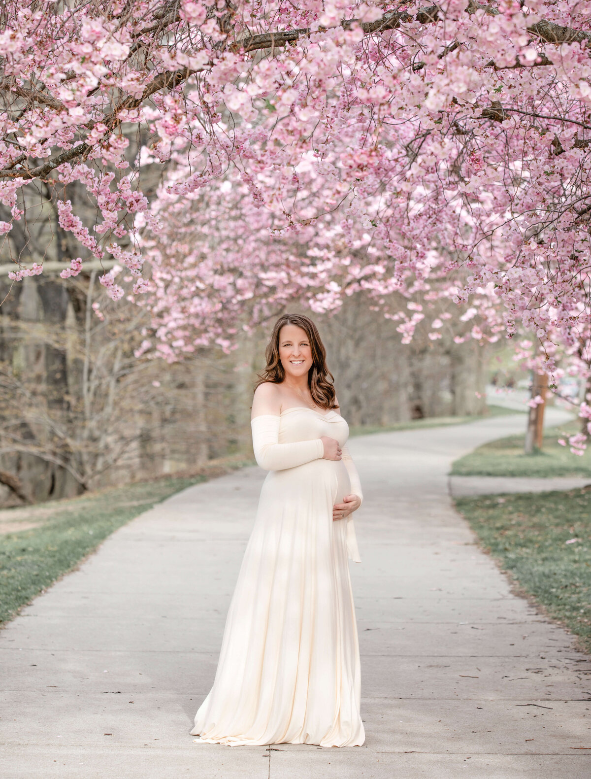 A young pregnant woman posing in front of beautiful cherry blossoms in Rochester NY