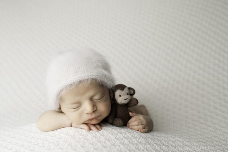 Newborn baby boy peacefully sleeping while gently holding a tiny plush monkey, creating an adorable and heartwarming scene