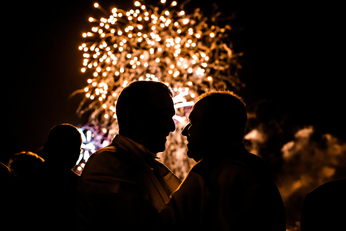 Fireworks light up the night sky and silhouette these two grooms on their wedding day at the Hilton Penns Landing.