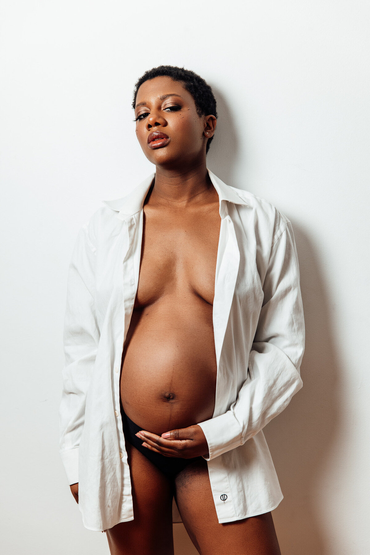 Pregnant Black woman with short hair in white button down shirt