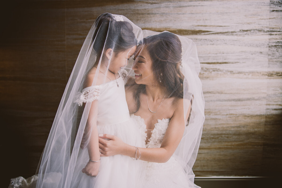 vietnamese christian bride share a  moment with the flower girl with the veil over both of their heads