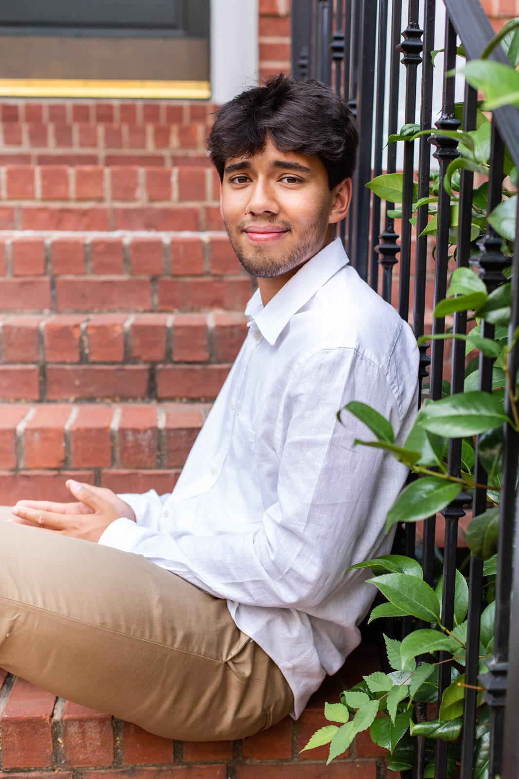 Urban high school senior boy sitting on house front steps wearing beige pants and a white shirt Atlanta GA