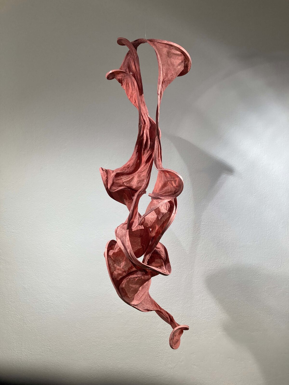 Sculptural form made from handmade abaca paper, twisted and flowing in organic curves, suspended against a neutral wall.