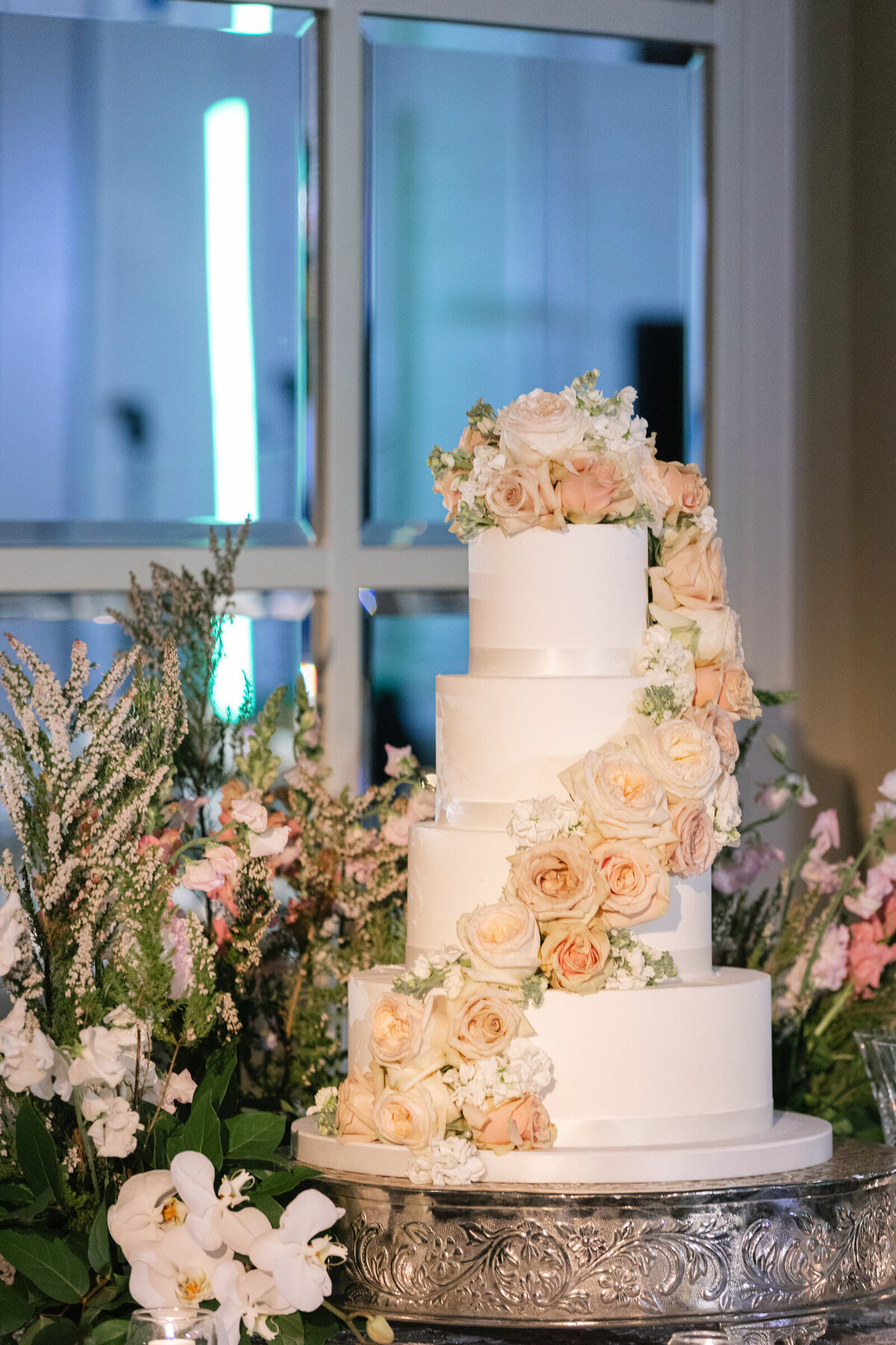 close up of a wedding cake at The Adolphus in Dallas decorated with blush roses and abundant floral details, highlighting the elegant reception design at this venue.