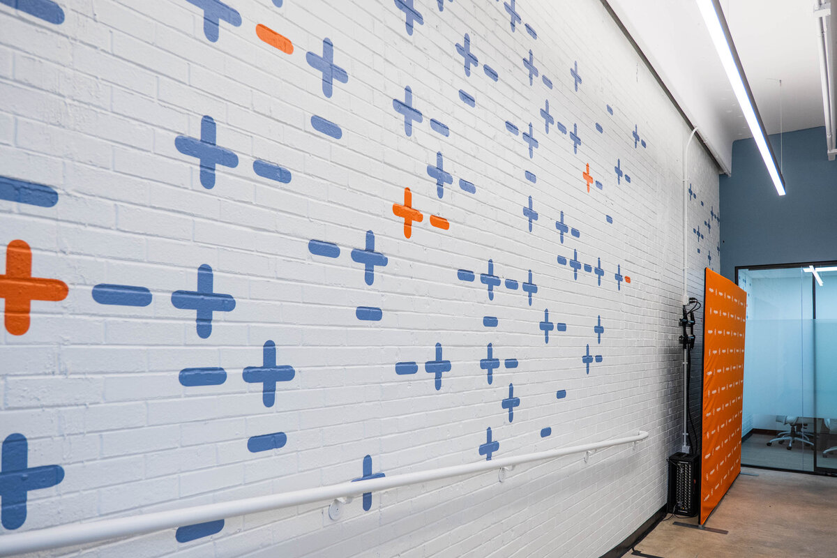 A white wall with blue and orange "+" and "-" painted on it 
