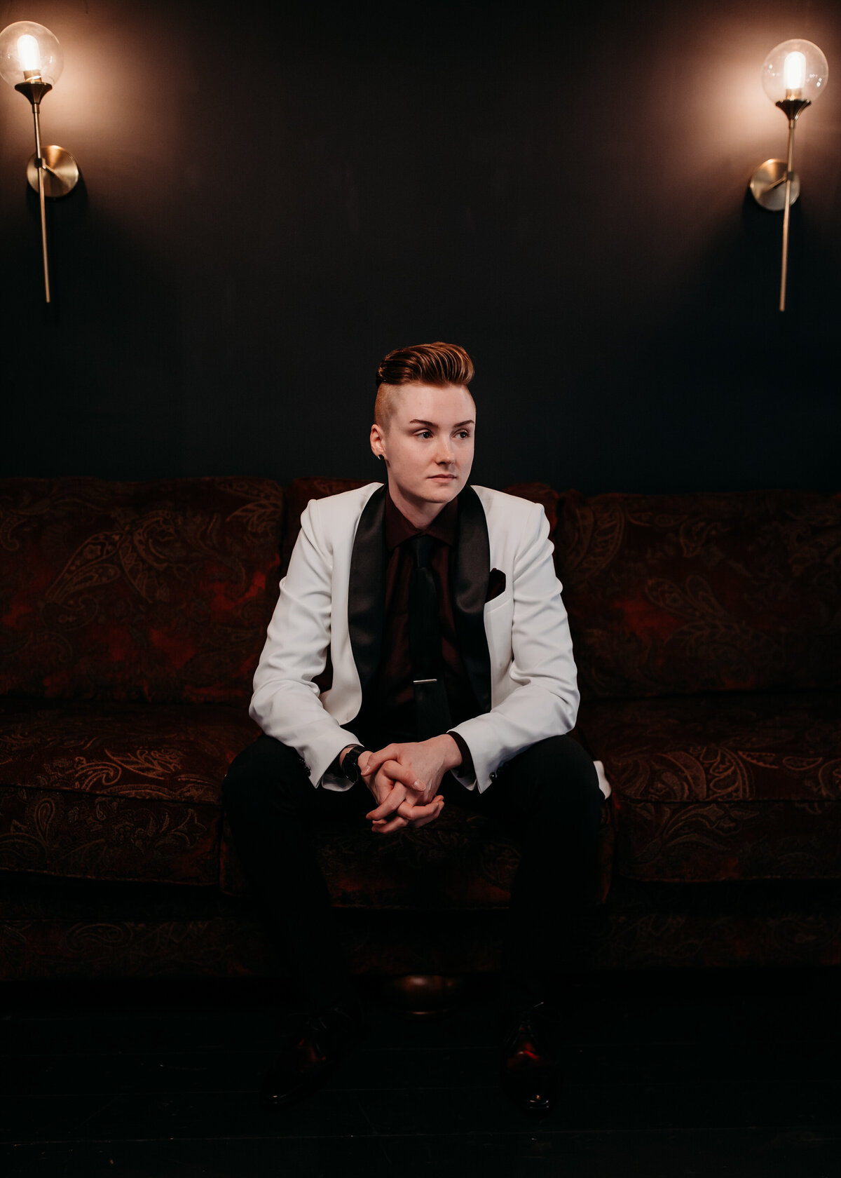 Person seated on a vintage couch in a stylish white jacket with black lapels