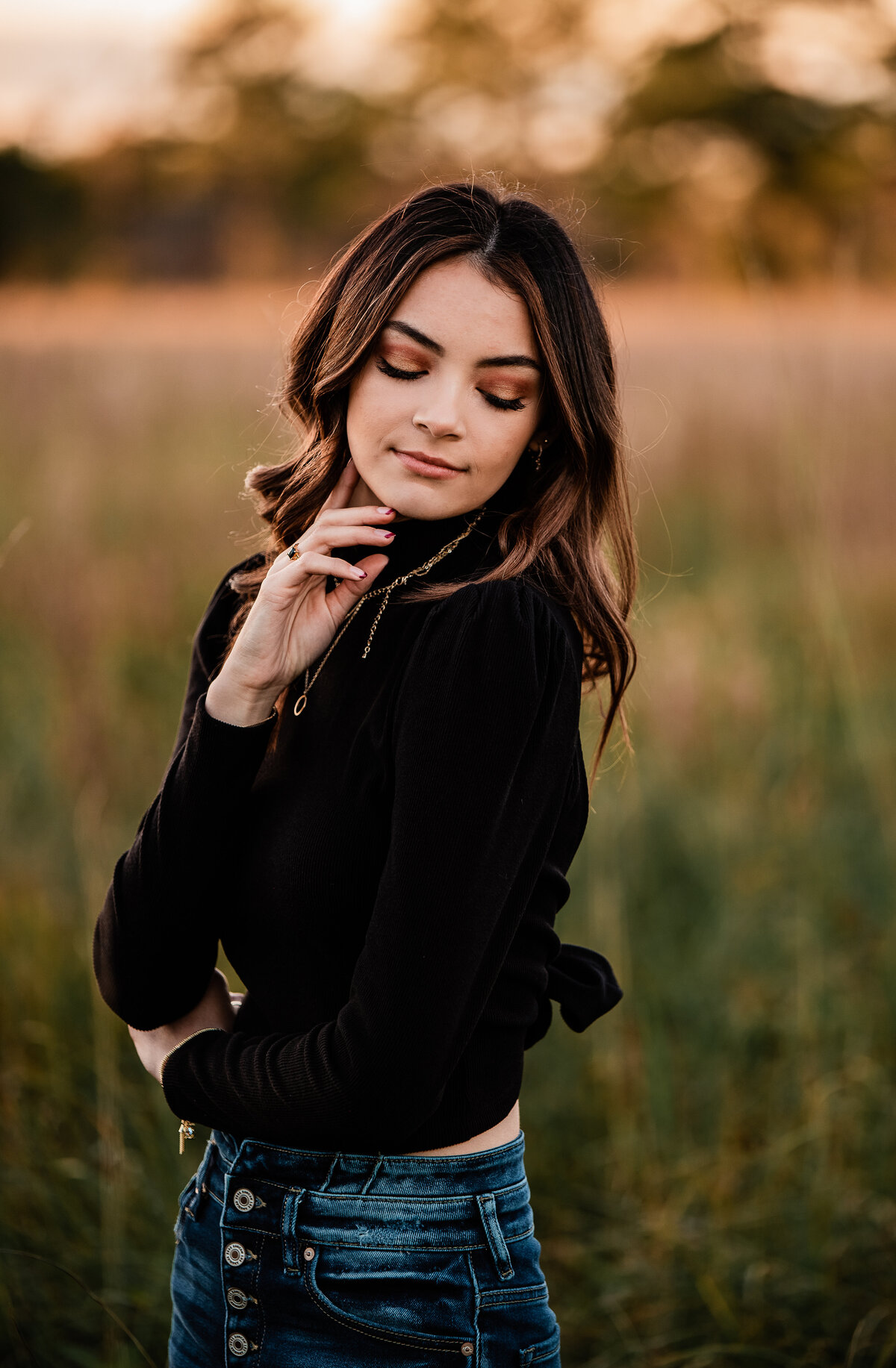 A young woman wearing a black turtleneck looks over her shoulder while standing in a long grass field at Jack Brooks Park.