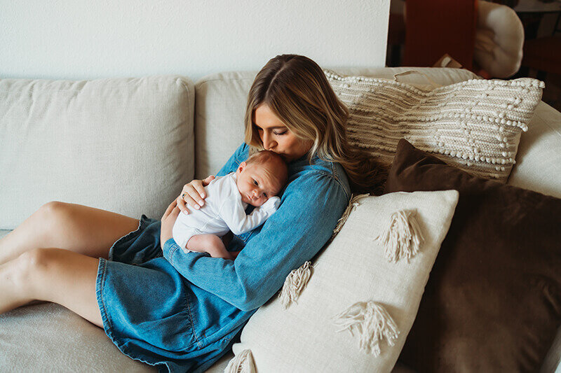 mom cuddles newborn baby boy while wearing a denim dress