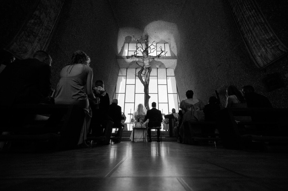 Wedding ceremony inside the Chapel of the Holy Cross in Sedona, with the couple seated before the altar, photographed by Arizona wedding photographers.