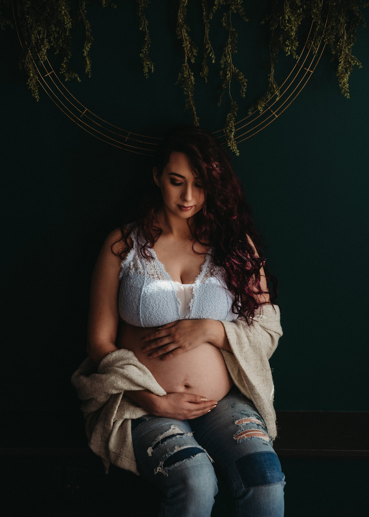 Pregnant woman holds belly in casual clothes in moody portrait.