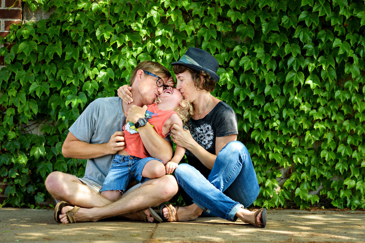 Parents kiss their laughing son in front of an ivy wall in Philly.