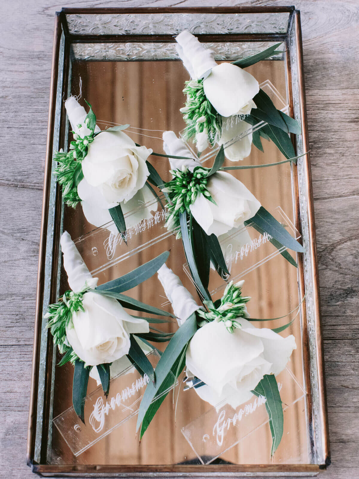 Five white flower boutonnieres with name labels on a tray for a wedding in Khayangan Estate, Indonesia. Image by Jenny Fu Studio