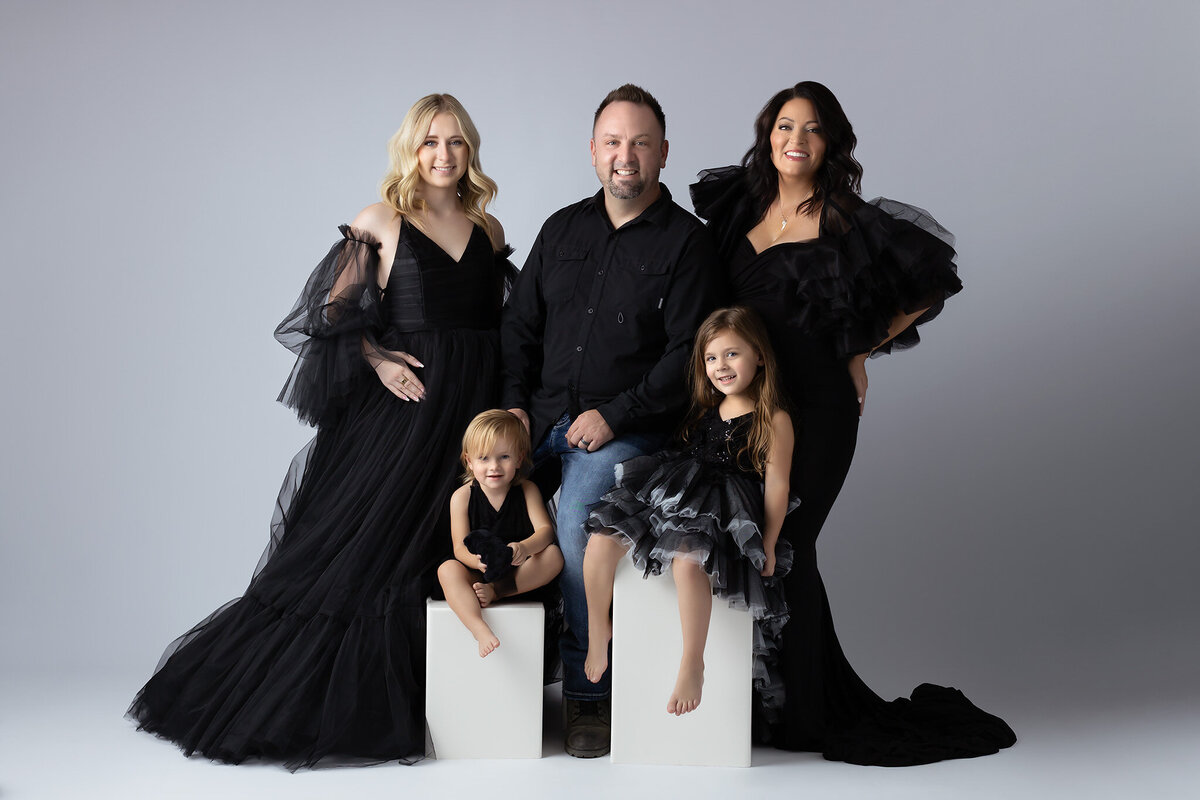 A family dressed in stylish black attire, with the father in black and the mother and daughters in chic black gowns, captured by a Dallas family photographer.