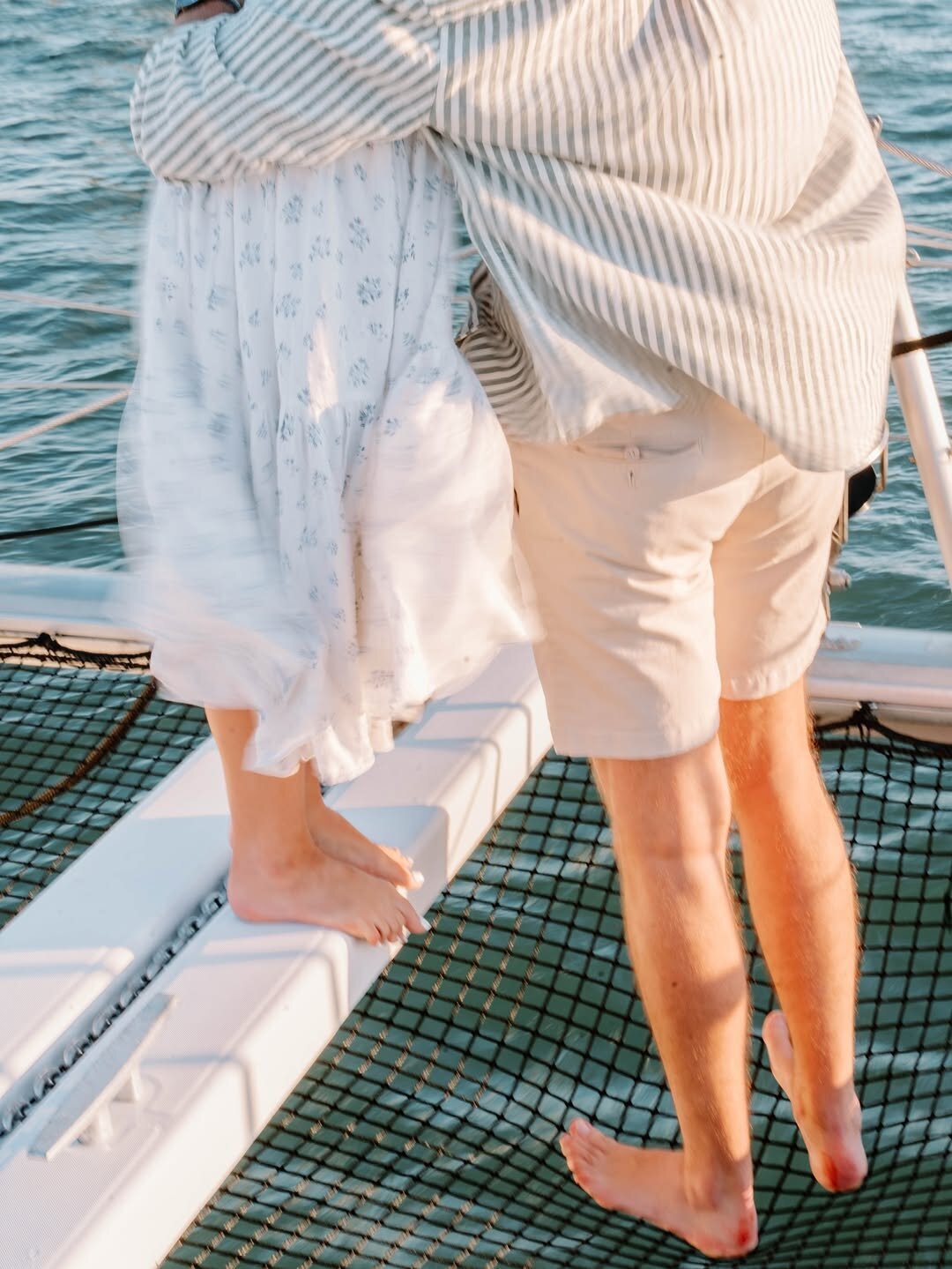 Wedding Photographer RI | A couple stands on a boat, with the woman's flowing white dress and the man's casual shorts. The ocean is visible in the background