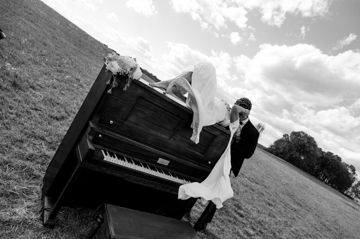 bride and groom sitting on a piano in a field