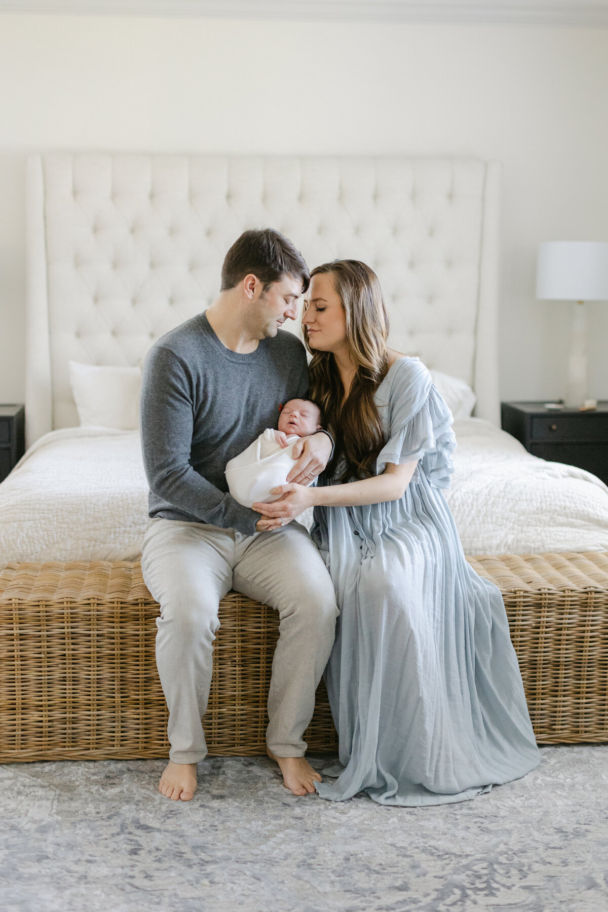 Mom and dad sitting at the foot of their bed holding their newborn baby during their in-home newborn session shot by Philadelphia Newborn Photographer Tara Federico