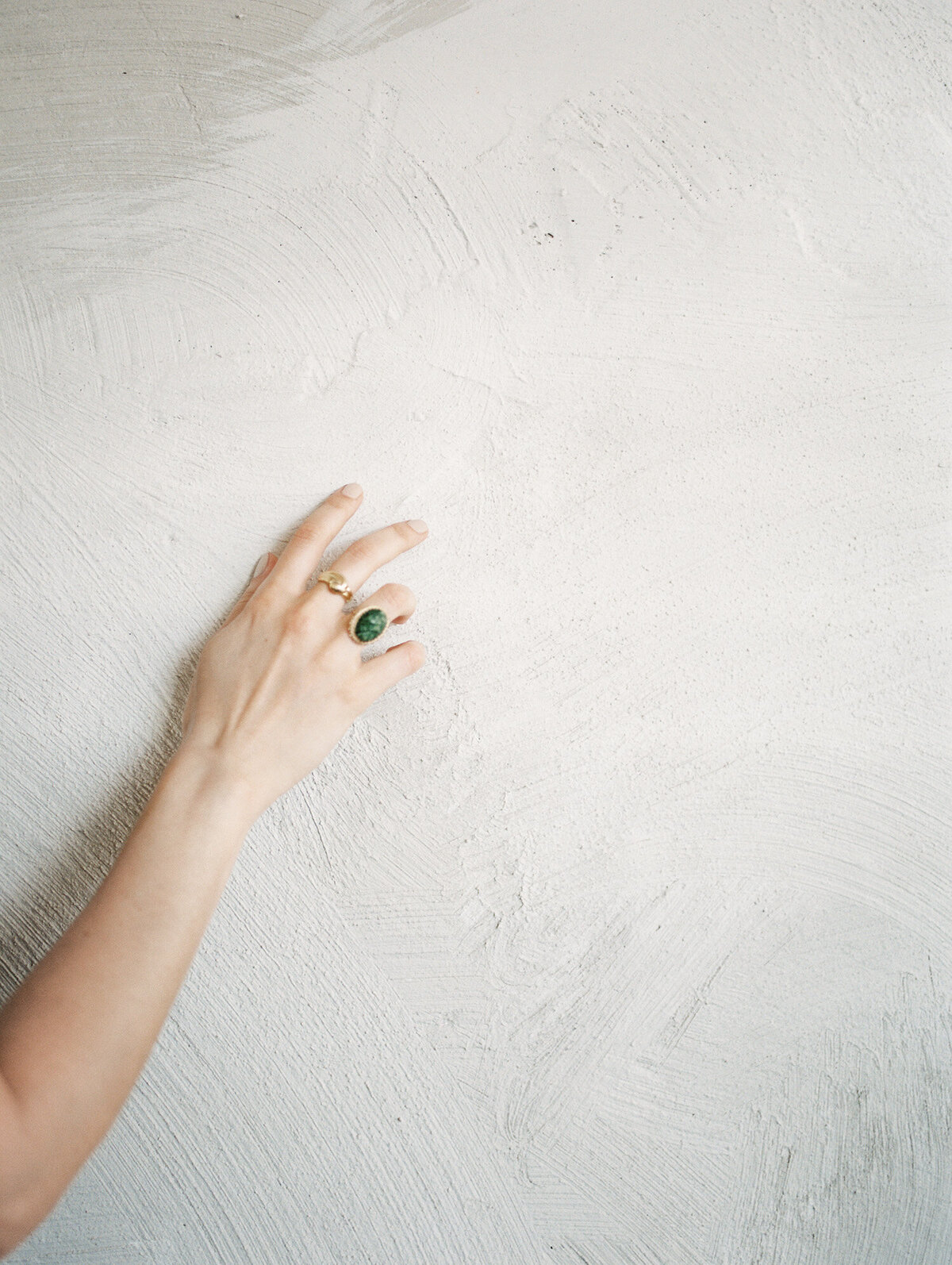 woman's hand with ornate gold rings, green stone, touches textured wall with warm tones, film brand photography