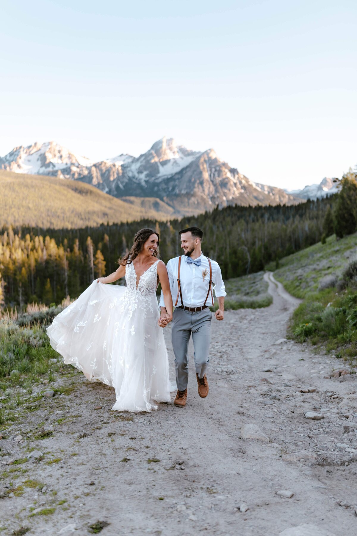 A bride and groom running up a dirt road in front of the Sawtooth Mountains in Idaho