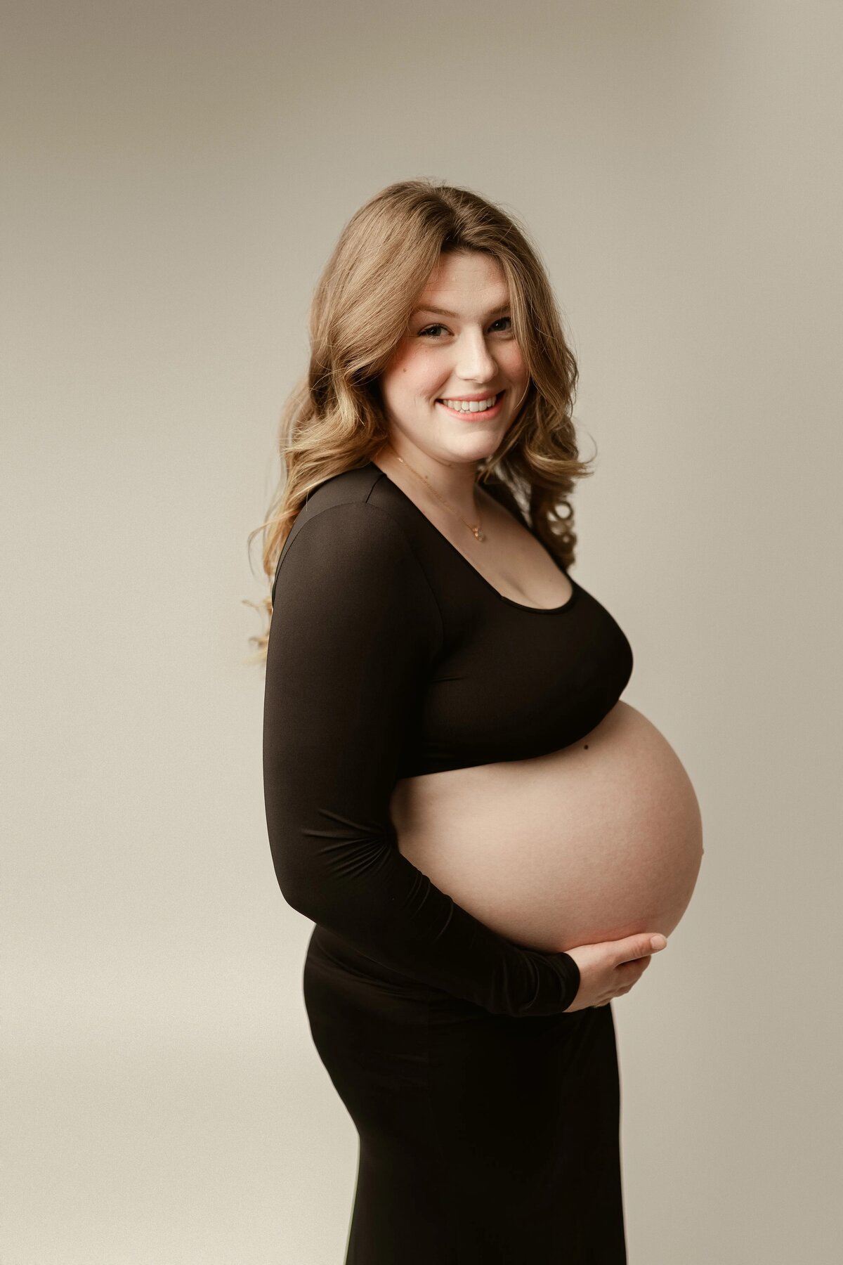 Profile shot of expecting mother in black dress holding belly in Maple Grove