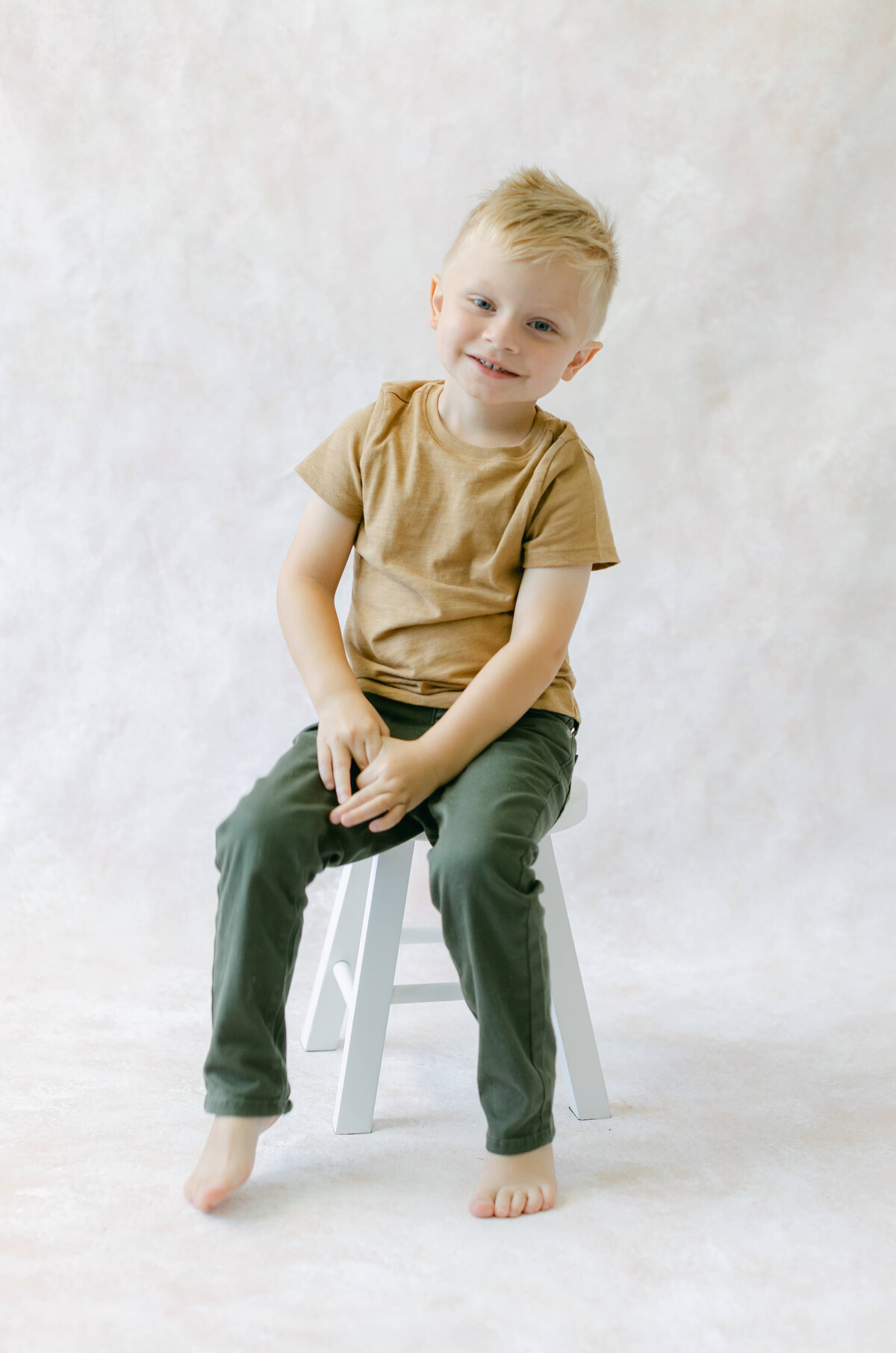 A young boy smiles while sitting on a white stool