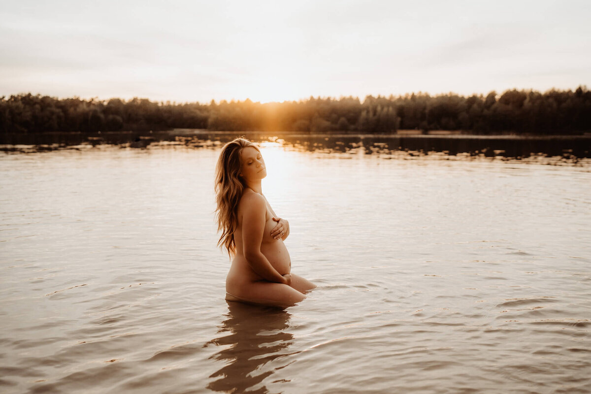 Zwangere vrouw tijdens een zwangerschapsshoot in het water bij zonsondergang