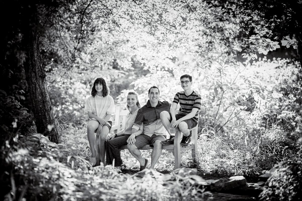 A family of four sitting on a bench in a wooded area.