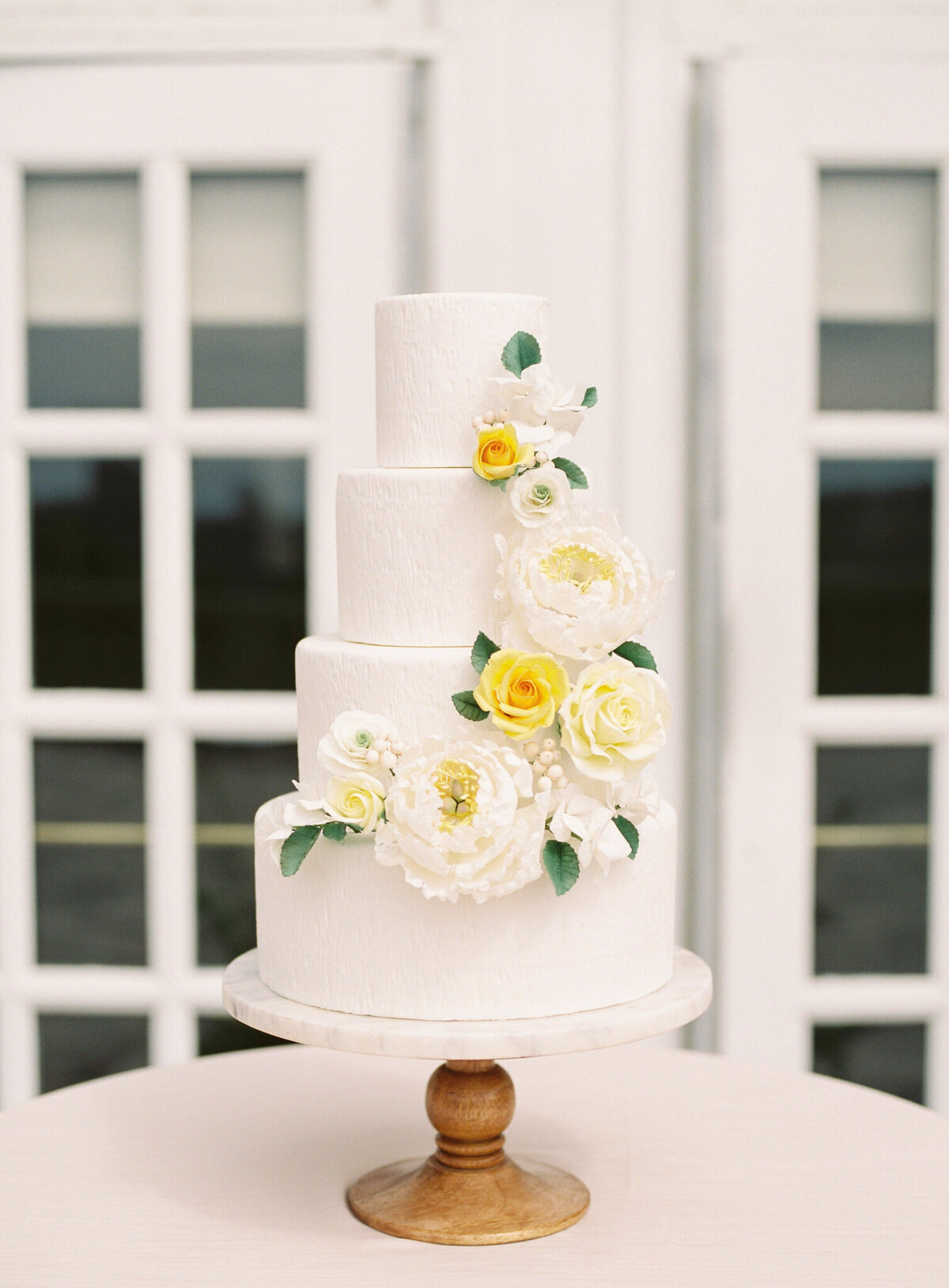 Beautiful professional four-tiered textured white wedding cake, with white and yellow cascading sugar roses, created by Brianne Gabrielle Cakes,  elegant cakes & desserts in Edmonton, AB, featured on the Brontë Bride Vendor Guide.