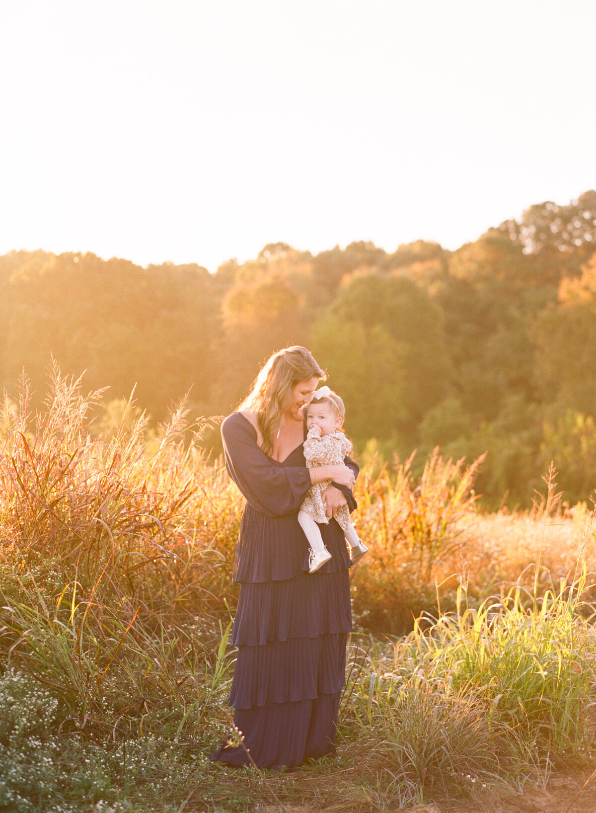 Mom holds baby daughter close as sun bathes them in this sunrise portrait at the NC Museum of Art. Image by Raleigh maternity photographer A.J. Dunlap Photography.