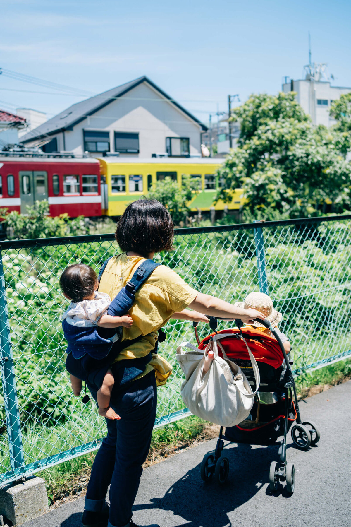 電車を眺めながらベビーカーとおんぶで散歩する親子