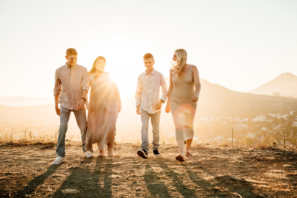 Backlit image at sunset of 4 older siblings walking on Bishpos Peak in San Luis Obispo