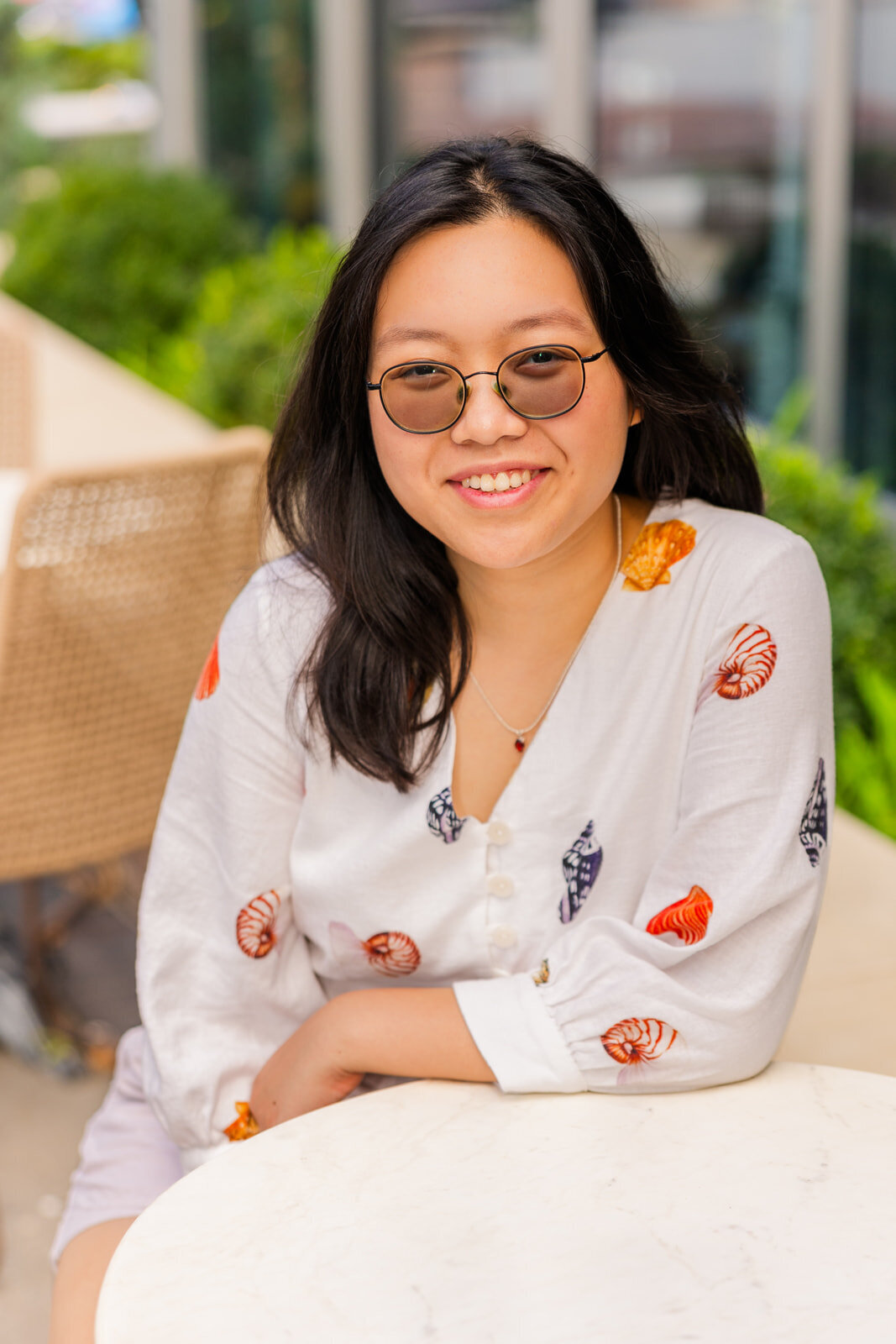 teenage girl wearing a patterned shirt sitting at a coffee table during senior photo session in Sandy Spring