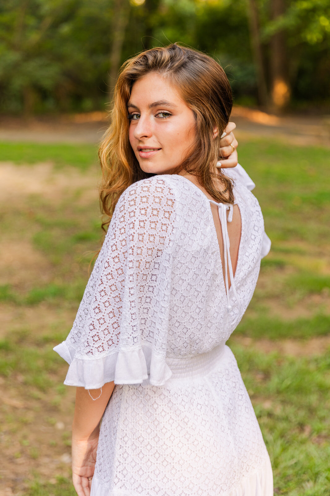 Summer high school senior photo session girl wearing a white dress looking behind her shoulder by photographer Laure Photography