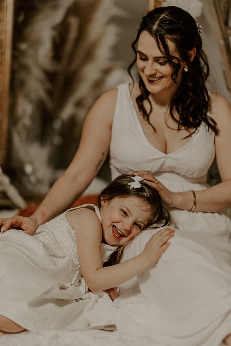 Petite fille allongée reposant sa tête sur les genoux de sa maman en robe blanche lors d'une séance photo à mon studio.