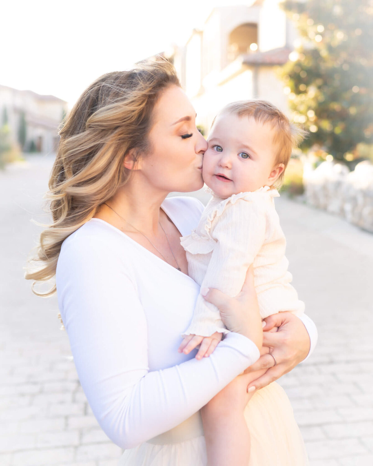 mom holding baby girl kissing her cheek as the wind blows her hair in a beautiful portrait in Adriatica village