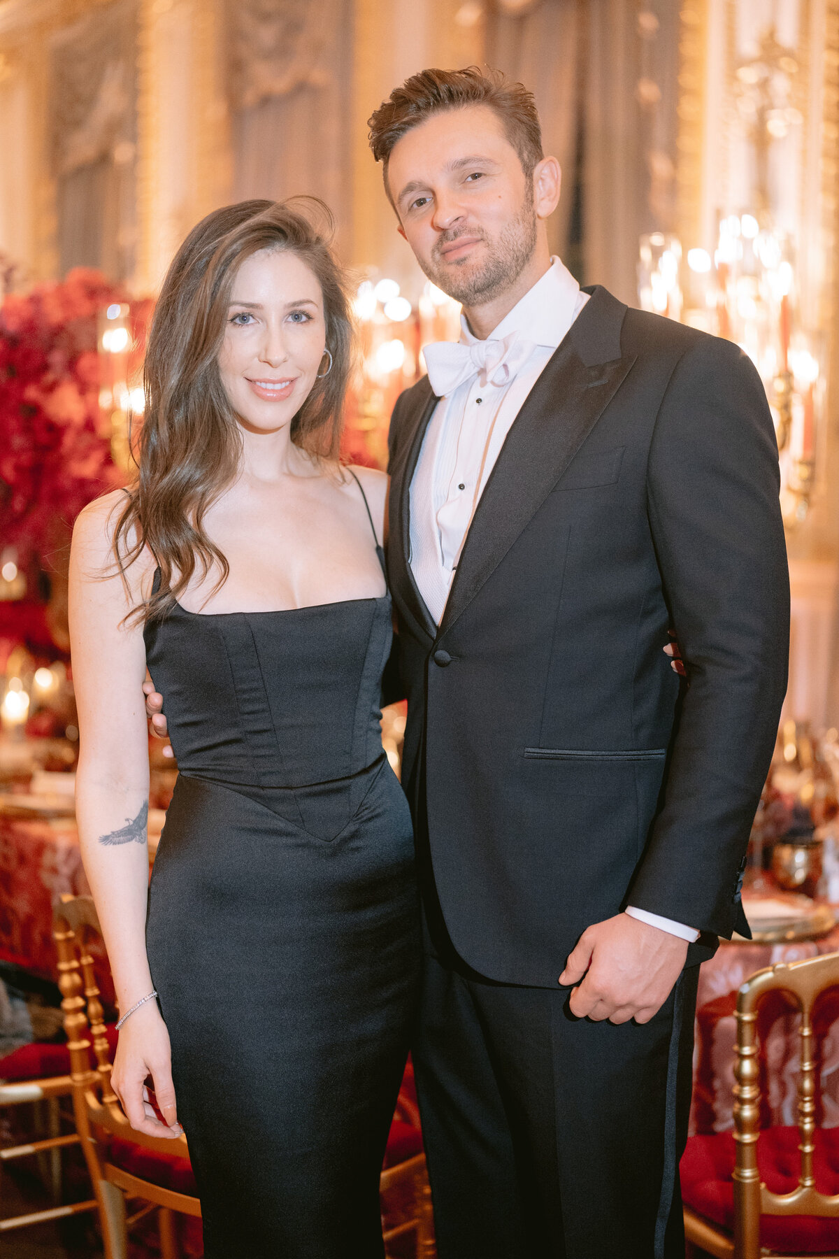 The stunning photo was taken at the luxurious Shangri La Hotel & Ritz Paris Hotel in Paris, France, capturing a couple dressed elegantly standing close together in a lavishly decorated room with chandeliers and floral arrangements. The woman is radiant in a form-fitting black gown, while the man exudes sophistication in a black tuxedo complemented by a white bow tie. The talented photographer Matteo Coltro skillfully captured the moment, showcasing the couple's joyous smiles at the camera. Additionally, Zen Film Works provided videography services to capture this beautiful moment on film.