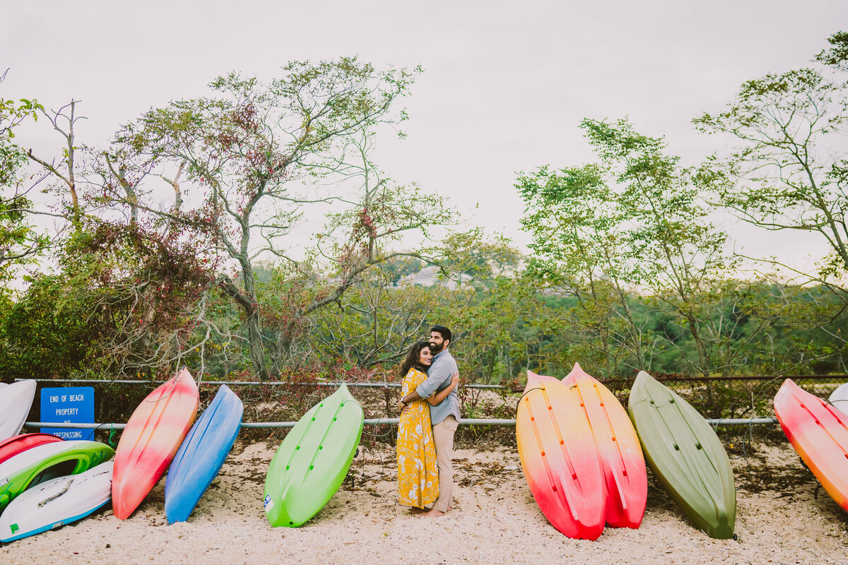 A couple embracing in between some colorful canoes at lloyd neck beach in ny
