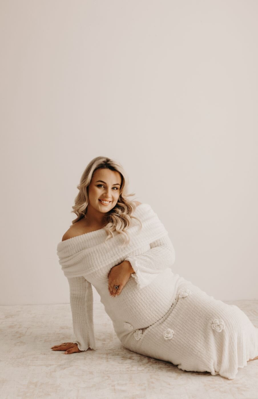 Smiling pregnant woman with blonde curls in a white textured dress during a maternity photoshoot
