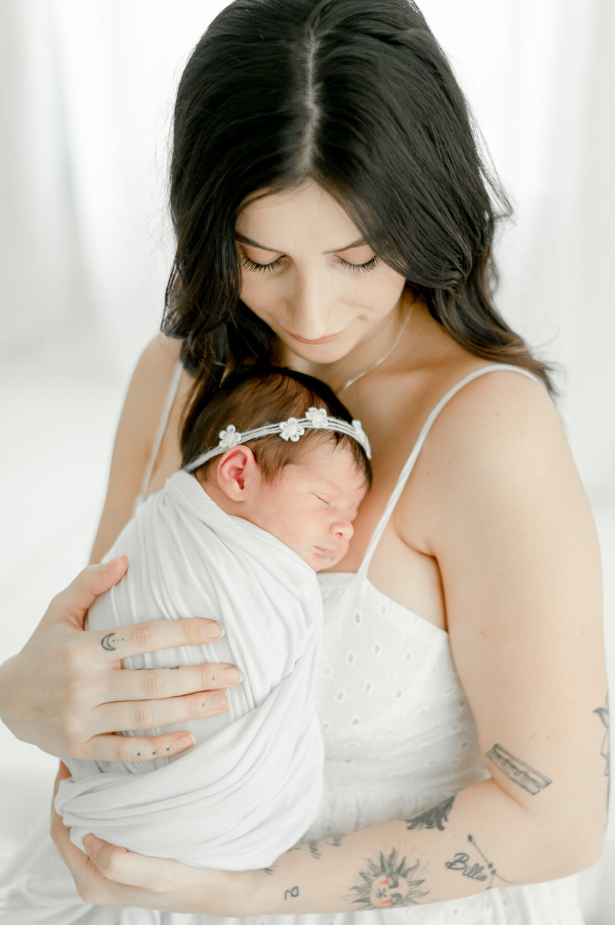 A mother with tattoos holds her sleeping baby for newborn photos In Kristie Lloyd’s Nashville newborn photographer studio