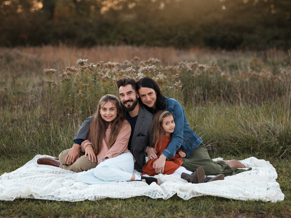 mom dad and two daughters posing in field for family photos 