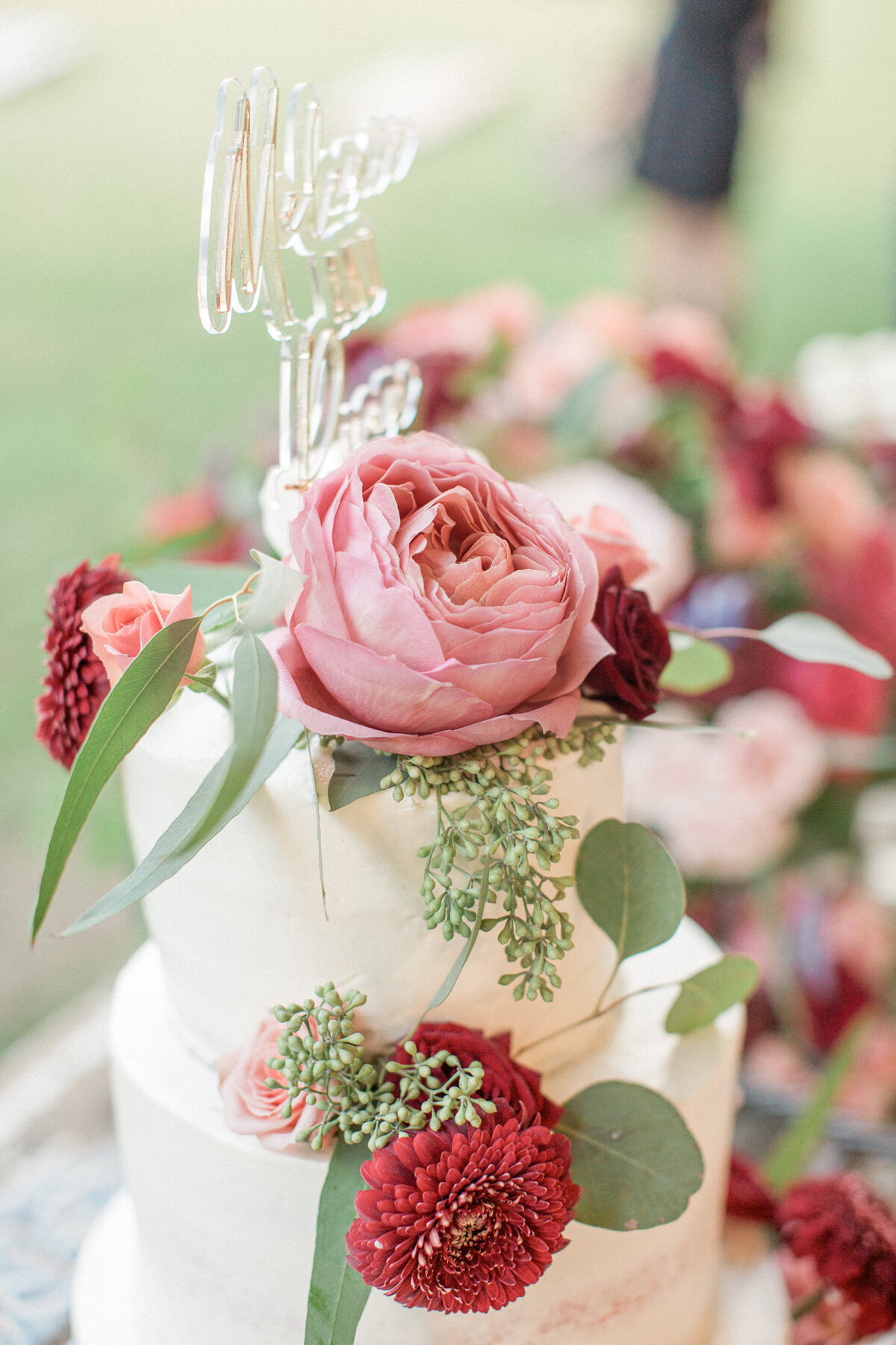 Close up of the wedding cake, topped with roses, carnations and eucalyptus