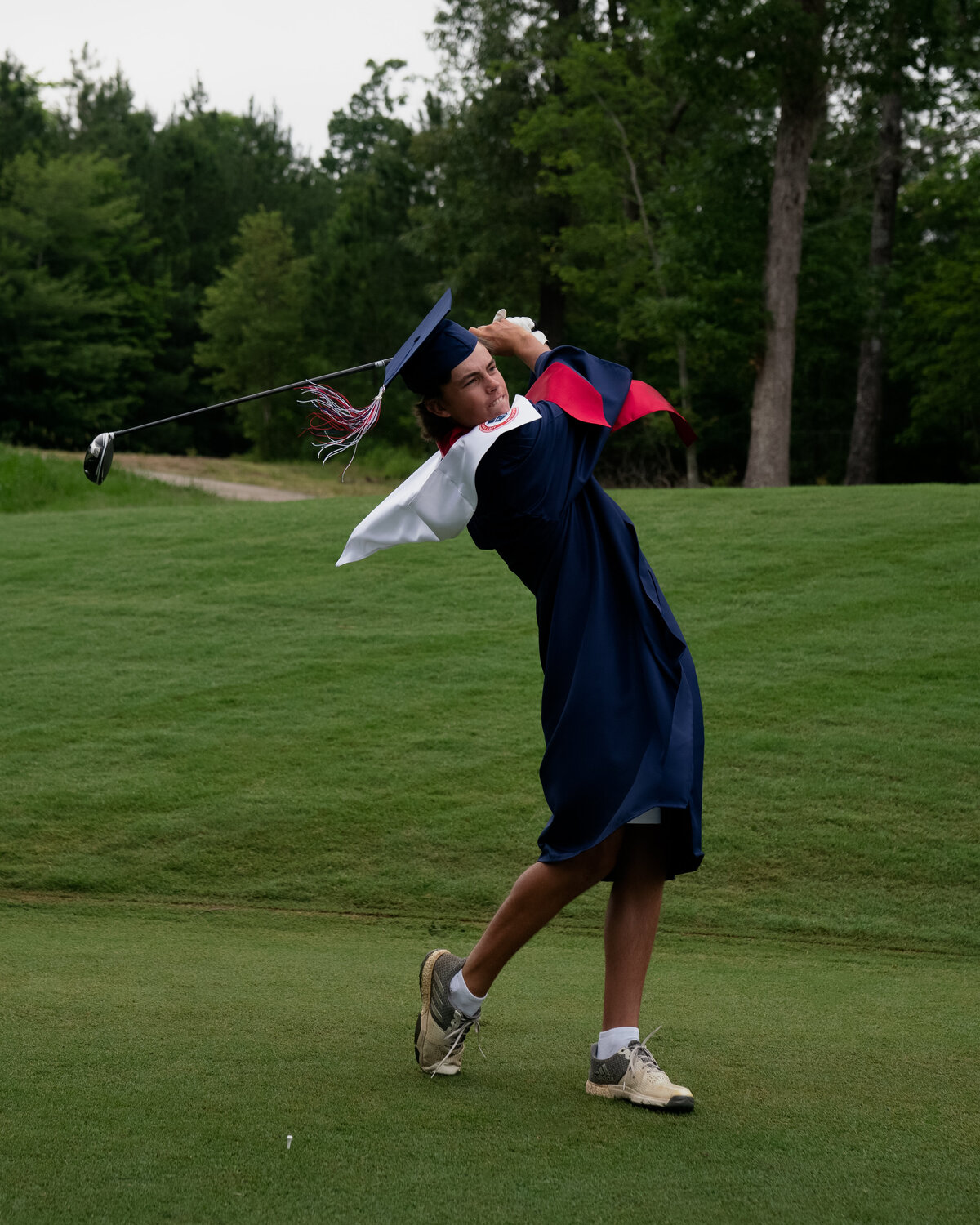 Garrett Risner swinging golf club in cap and gown on a dark dreary day. Captured at The Club at 12 Oaks Holly Springs, NC in Spring 2020.