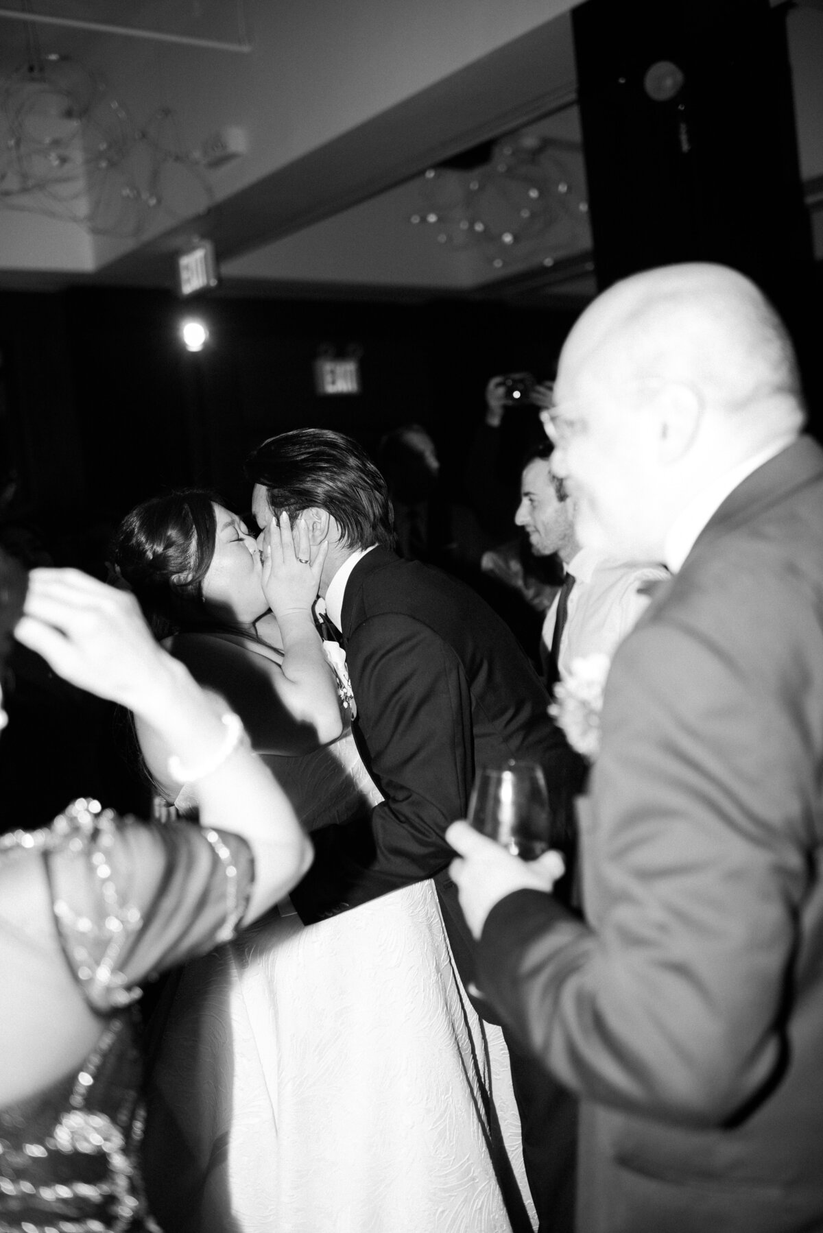 Bride and groom kiss on the dance floor surrounded by friends