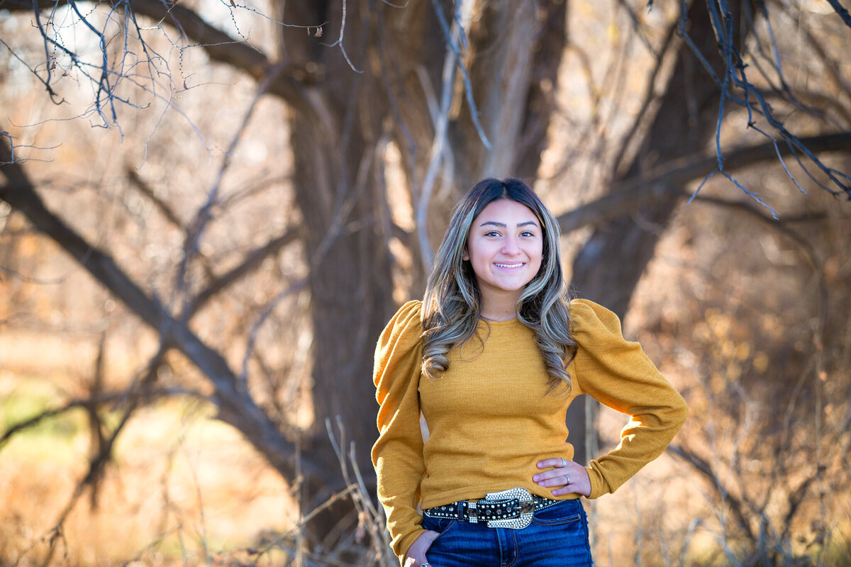 senior girl standing against dead trees in yellow shirt
